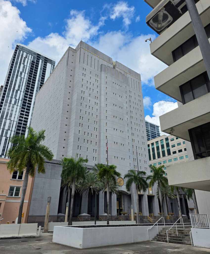 The Federal Detention Center Miami, photographed from street level with palm trees, flags and the building facade.