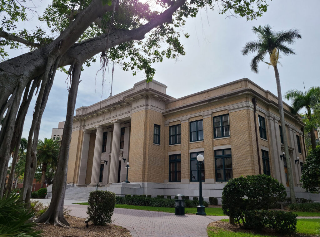 The historic Lee County Courthouse in downtown Fort Myers, Florida, framed by trees and palms.